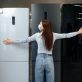 Young happy woman in mask leaning on her new refrigerator in a shopping mall
