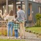 Happy family. View from back of man woman with child and girl standing together hugging and admiring their cozy home on fine autumn day
